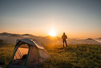 A camper enjoys the sunrise in a mountain setting with a tent. Perfect nature escape. HD wallpaper