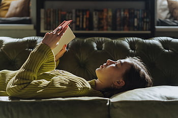 A young woman lies on a sofa reading a book, enjoying a peaceful indoor moment. HD wallpaper