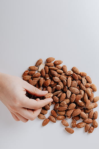 A hand reaches for raw almonds spread on a white surface, emphasizing healthy snacking. HD phone wallpaper