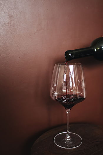 Close-up of red wine being poured into a glass against a warm, brown background, creating a luxurious atmosphere. HD phone wallpaper