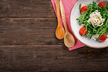 A vibrant arugula salad with tomatoes and cheese on a rustic wooden table, perfect for healthy dining. HD wallpaper