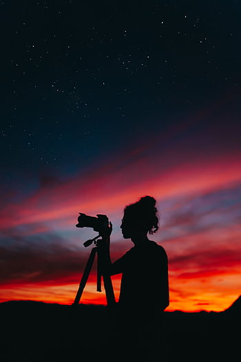 Silhouette of a grapher capturing the starry sky during a colorful sunset, creating a dramatic and artistic scene. HD phone wallpaper