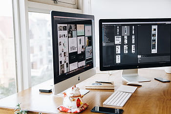 A sleek modern office setup featuring dual monitors, Apple devices, and creative decor in an indoor workspace. HD wallpaper