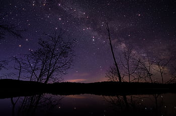 A tranquil night view of a starry sky reflecting over a calm lake. HD wallpaper