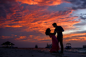 Silhouetted couple sharing a romantic moment on the beach during a stunning sunset. HD wallpaper
