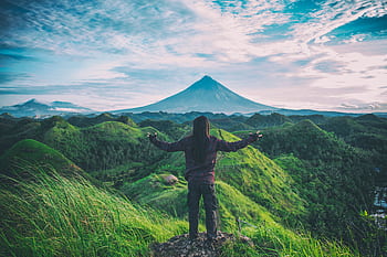 A person enjoys an expansive view of Mt. Mayon amidst lush green hills in Bicol, Philippines. HD wallpaper