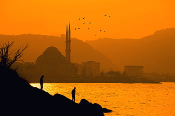 Silhouetted figures and mosque with birds at a vibrant Korgan sunset. HD wallpaper