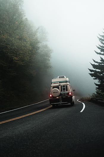A camper van travels through a foggy rural road, creating a serene scene for adventure. HD phone wallpaper