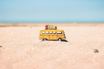 A toy van on a sandy beach evokes summer travel and vacation vibes. HD wallpaper