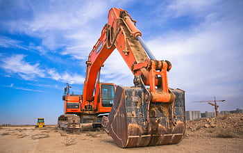 A large orange excavator working on a construction site under a blue sky. HD wallpaper