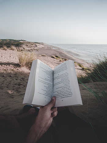 A person enjoys reading a book while relaxing on a serene beach, with the ocean in view. HD phone wallpaper
