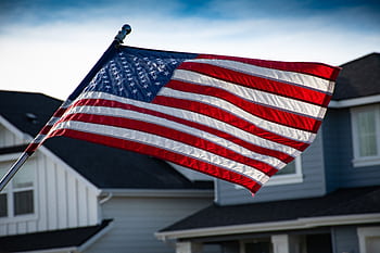 A close-up of the American flag waving in front of a suburban house, symbolizing patriotism. HD wallpaper