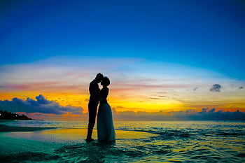 Silhouette of a couple kissing on a tropical beach at sunset, showcasing romance and tranquility. HD wallpaper