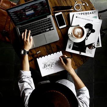 Top view of a creative workspace with laptop, coffee, and hand lettering for design inspiration. HD phone wallpaper
