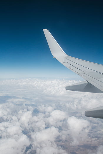 High-altitude view of airplane wing with white clouds and blue sky backdrop, perfect for travel themes. HD phone wallpaper
