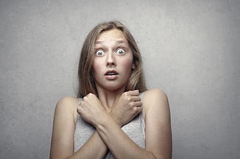 Portrait of a surprised woman with wide eyes and crossed arms against a gray background. HD wallpaper