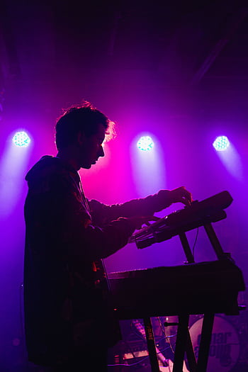 A DJ mixing music on stage with vibrant purple lighting creating a moody atmosphere. HD phone wallpaper