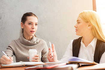 Two women engaging in a professional conversation over coffee and notes. HD wallpaper