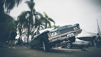 A vibrant lowrider car with palm trees and people at an outdoor car show. HD wallpaper