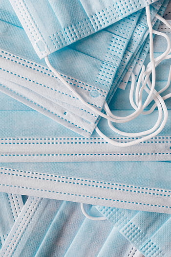 A close-up view of a stacked pile of blue surgical face masks, symbolizing health and safety measures. HD phone wallpaper