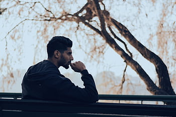 Man in deep thought sitting on a bench in a serene autumn park setting. HD wallpaper