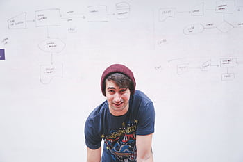 Smiling young man stands in front of a whiteboard with flowchart diagrams, creativity and planning concept. HD wallpaper