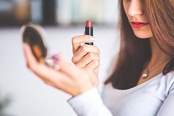 Close-up of woman applying red lipstick while holding a compact mirror. HD wallpaper