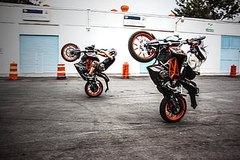 Two motorcyclists performing wheelies on a road in Mexico City, showcasing thrilling stunts. HD wallpaper