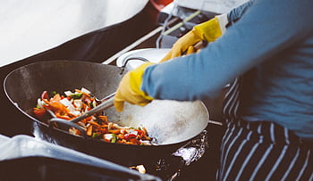 A chef stir-frying vegetables in a wok, showcasing vibrant fresh ingredients. HD wallpaper