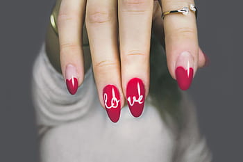 Vibrant red nails with 'love' art on a woman's hand, showcasing elegant style and design. HD wallpaper