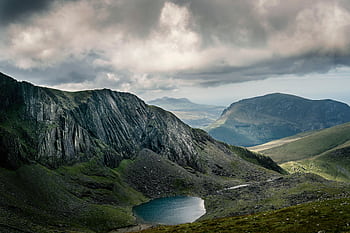 Breathtaking view of rocky mountains and serene lake under a dramatic cloudy sky. HD wallpaper