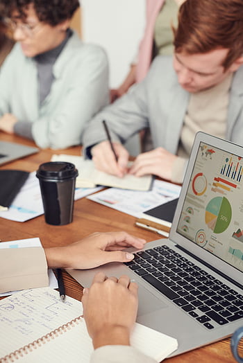 Professionals working together in an office setting with charts on a laptop for data analysis. HD phone wallpaper