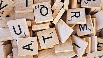 Close-up of wooden Scrabble tiles showcasing letters and numbers for word games. HD wallpaper