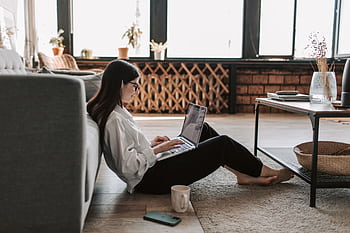 A young woman working from home using a laptop in a relaxed living room setting. HD wallpaper