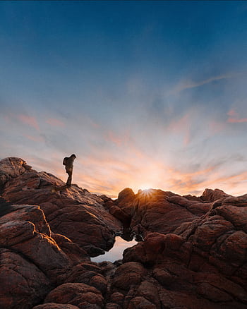 A silhouette of a hiker appreciating a stunning sunset over a rugged rocky terrain, embodying adventure and solitude. HD phone wallpaper