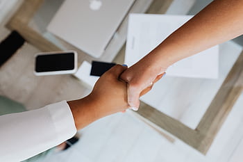 Two people shaking hands over a desk with modern tech, symbolizing a successful business agreement. HD wallpaper