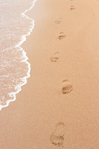 Footprints on a sandy beach beside ocean waves, perfect for summer themes. HD phone wallpaper