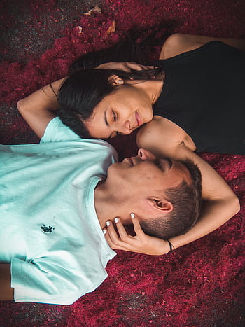 Young couple embracing on vibrant red grass, displaying intimacy and relaxation. HD phone wallpaper