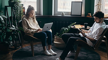 A couple working remotely in a stylish home office with plants and modern decor. HD wallpaper