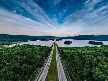 A breathtaking aerial shot of a highway running through lush forests beside a serene lake at sunset. HD wallpaper
