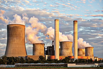 View of a power plant with smoke emissions under a cloudy sky, depicting industrial energy production. HD wallpaper