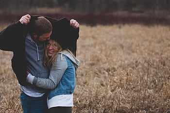 A couple shares a warm embrace under a coat in a rustic autumn field, expressing love and togetherness. HD wallpaper