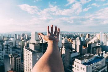 An outstretched hand reaching towards a sunny cityscape, capturing the vibrant skyline and skyscrapers. HD wallpaper