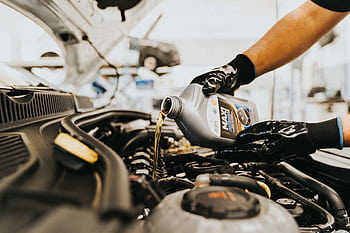 Close-up of a mechanic pouring engine oil into a car engine in an auto repair shop. HD wallpaper