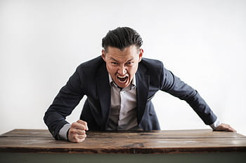 Frustrated businessman in a suit yelling at camera, expressing anger and stress. HD wallpaper