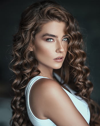 A striking portrait of a woman with luscious curly hair and a fierce expression in a white top. HD phone wallpaper