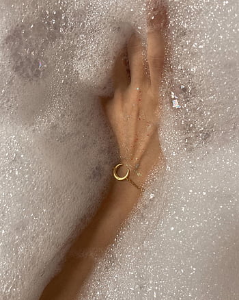 A woman's hand with a bracelet submerged in a bubbly bathtub, capturing serenity and self-care. HD phone wallpaper