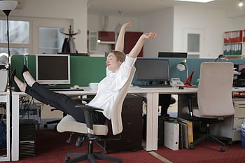 Young woman in office relaxing with feet on desk, embodying workplace ease. HD wallpaper