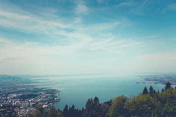 A breathtaking panoramic view of the ocean, city, and lush green forest under a vibrant blue sky. HD wallpaper