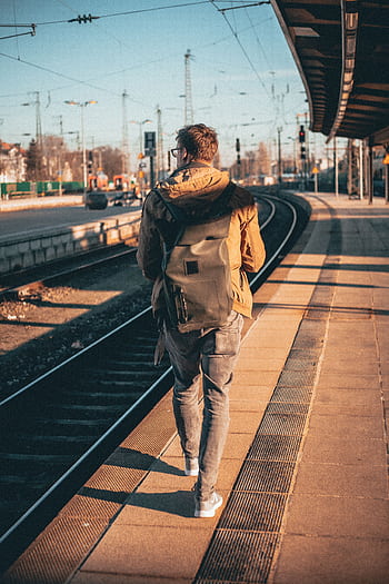 A man with a backpack walks along a train platform, capturing a journey moment in urban daylight. HD phone wallpaper